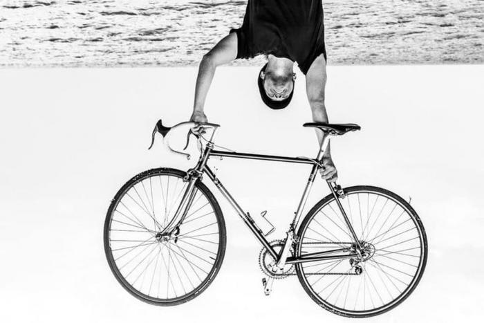 fotografia b/n uomo che solleva in alto bicicletta da corsa